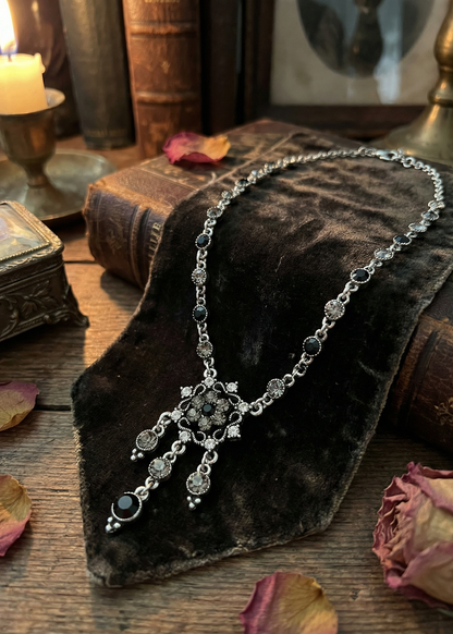 Filigranes Gothic Collier mit schwarzen und grauen Strasssteinen auf dunklem Stoff arrangiert.