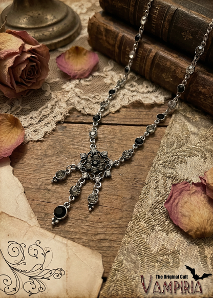 Gothic Halskette mit ornamentalem Mittelteil und hängenden Elementen auf Holztisch mit Vintage-Dekoration.