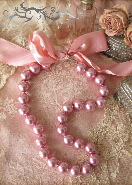 Rosa Perlenkette mit großen Perlen und breitem rosa Satinband auf rosafarbenem Stoff mit Spitze, Rosen und Flakons.