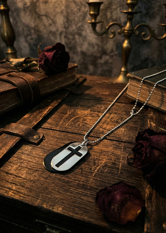 Zweilagiger Anhänger an Kugelkette mit schwarzer unterer Plakette und silberfarbener oberer Plakette mit ausgestanztem Kreuz auf dunklem Holztisch mit Büchern und Rosen.