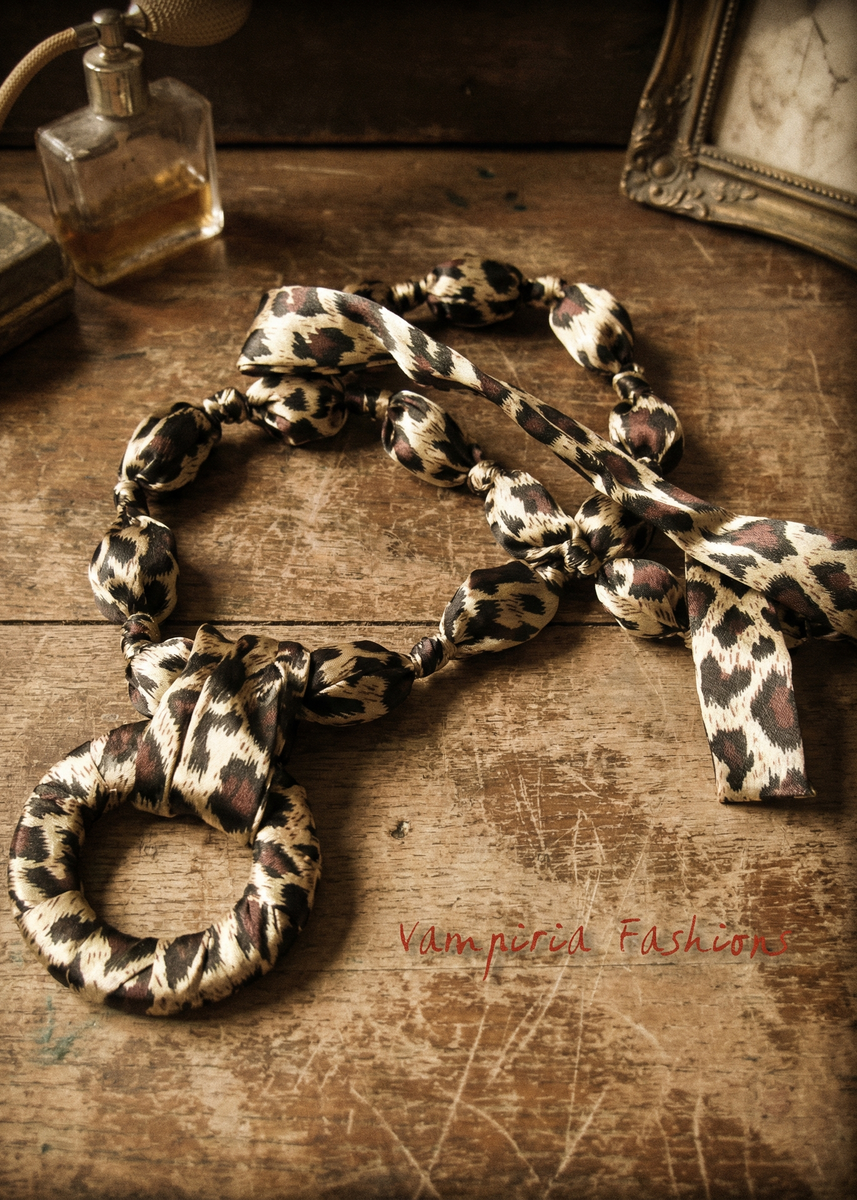 Leo-Satin-Halsschmuck auf Holztisch, kombinierter Halsschmuck aus Halstuch und stoffüberzogener Kette mit großem Ring-Anhänger und langem Satinband.