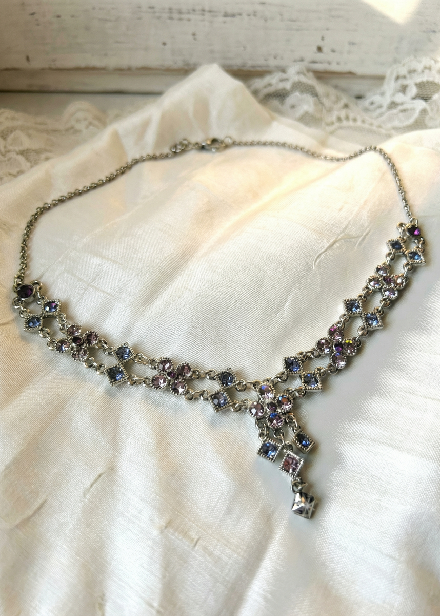 Silberfarbenes Vintage-Collier mit rosafarbenen und fliederfarbenen Strasssteinen auf hellem Stoff, mit filigranem Mittelanhänger und Karabinerverschluss.