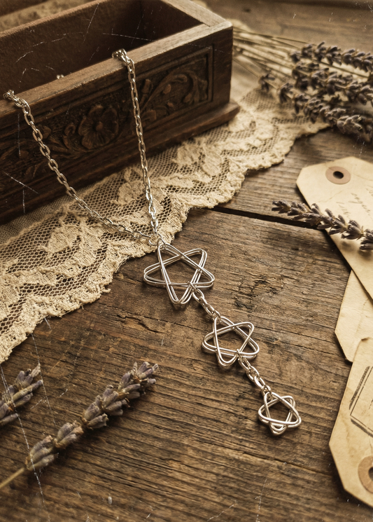 Silberfarbenes Collier mit drei offenen Stern-Anhängerformen auf Holztisch mit Spitze und Lavendel.