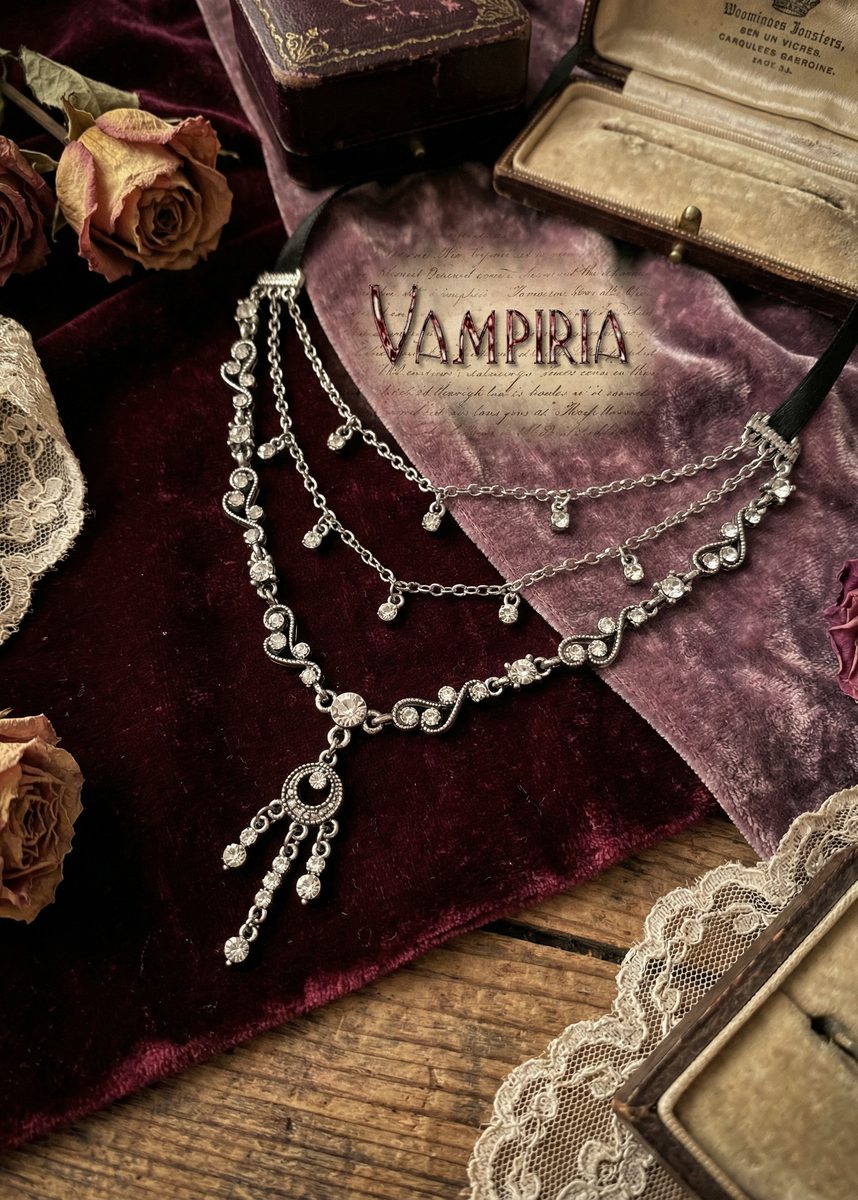 Vintage Collier mit silberfarbenen Ornamenten, klaren Kristallsteinen und mehreren Kettenreihen, auf dunkelrotem Samt drapiert, mit Rosen, Spitze und Schmuckschatullen im Hintergrund.
