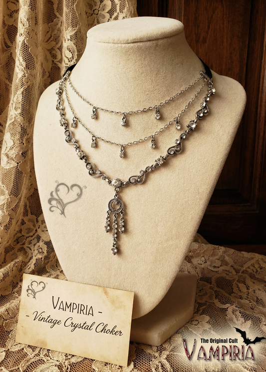 Mehrreihiges silberfarbenes Vintage-Crystal-Collier mit kleinen hängenden Kristallsteinen und zentralem Anhänger, präsentiert auf einer cremefarbenen Schmuckbüste vor Spitzentextil und Holzpaneel.