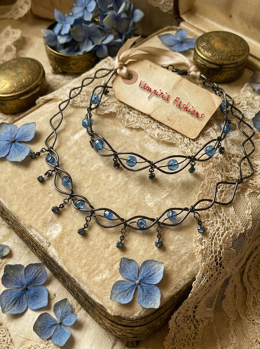 Dunkles Collier mit blauen Kristallperlen auf heller Unterlage mit blauen Blüten und Vintage-Dekoration.