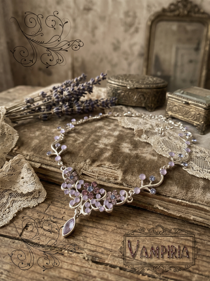 Florales Collier in Silberoptik mit lilafarbenen Steinen auf altem Buch mit Spitze und Lavendel; unten rechts ist der Schriftzug „Vampiria“ zu sehen.
