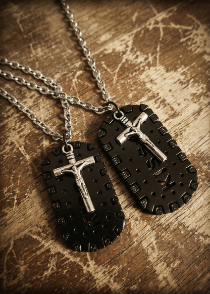 Zwei schwarze Plaketten-Anhänger mit silberfarbenem Kreuz und silberfarbenen Ketten auf einer Holzoberfläche.