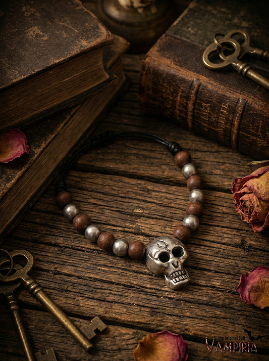 Halskette mit Totenkopf-Anhänger in Silberoptik und braunen Holzperlen auf rustikalem Holztisch zwischen alten Büchern, Schlüsseln und getrockneten Rosenblättern; unten rechts Schriftzug „Vampiria“.
