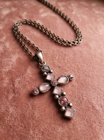 Kreuzanhänger im Antikdesign mit rosa und roséfarbenen Steinen an dunkler Gliederkette auf rosafarbenem Samtstoff.