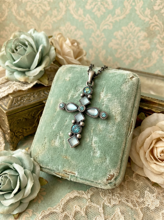 Kreuzanhänger im Antikdesign mit mintfarbenen und türkisfarbenen Steinen an dunkler Gliederkette auf mintgrünem Samtetui zwischen künstlichen Rosen, Spitze und dekorativer Vintage-Umgebung.