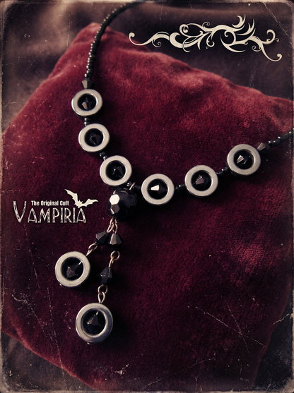Nahaufnahme eines schwarzen Y-Colliers mit runden Hämatit-Ringen und schwarzen Perlen auf dunkelrotem Samt; links Schriftzug „The Original Cult Vampiria“.