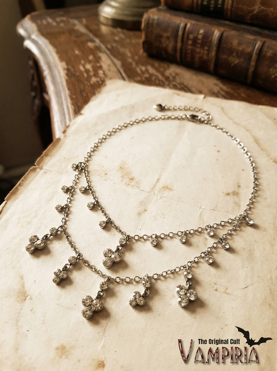 Filigranes Crystal-Collier mit funkelnden Anhängern auf hellem Papieruntergrund, daneben Bücher im Hintergrund.