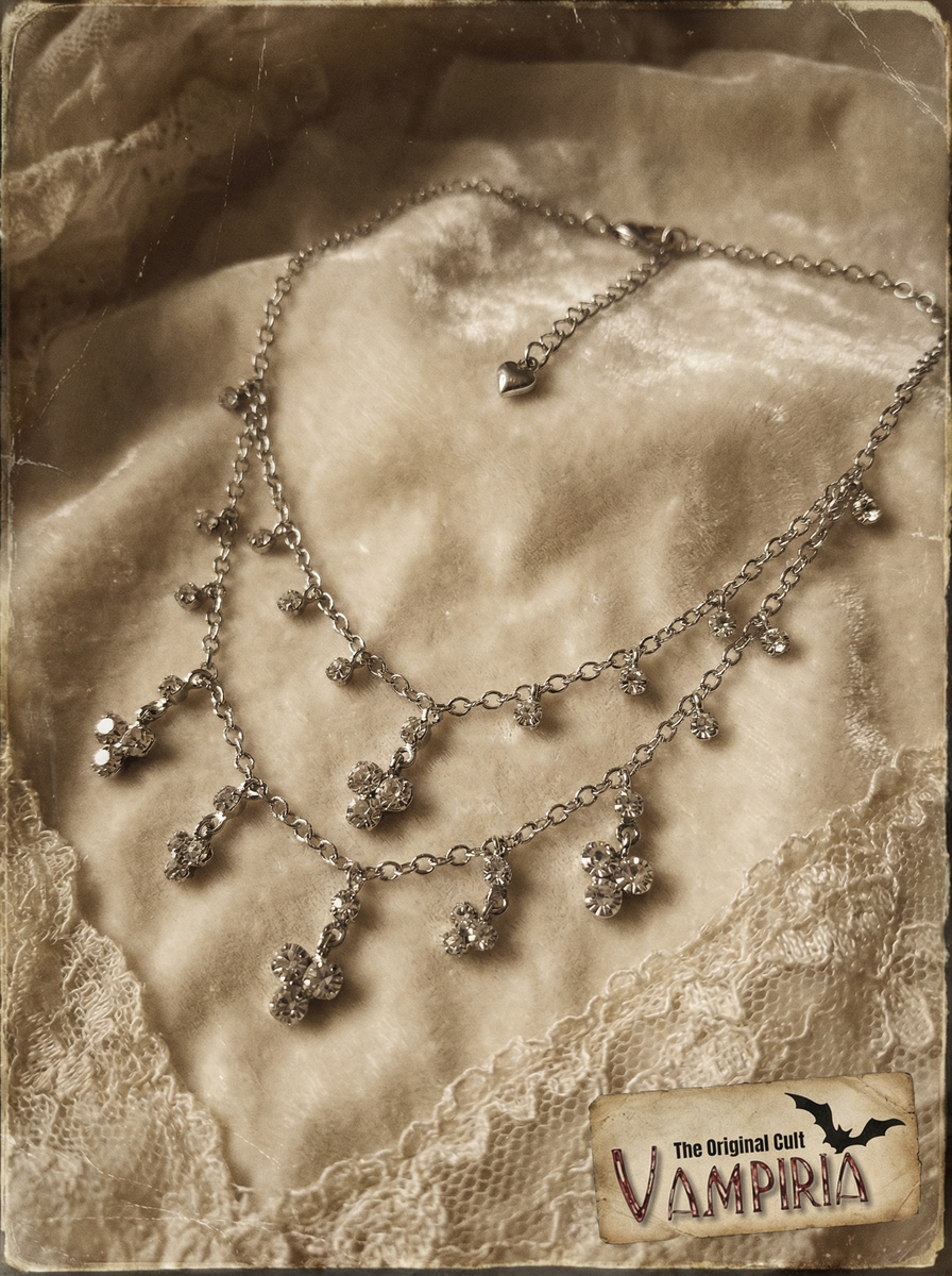 Mehrreihiges silberfarbenes Collier mit Crystal-Anhängern auf hellem Samtstoff im Vintage-Stil, mit Spitzenstoff und Vampiria-Logo im Bild.