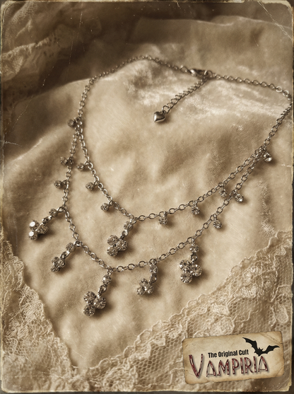 Mehrreihiges silberfarbenes Collier mit Crystal-Anhängern auf hellem Samtstoff im Vintage-Stil, mit Spitzenstoff und Vampiria-Logo im Bild.