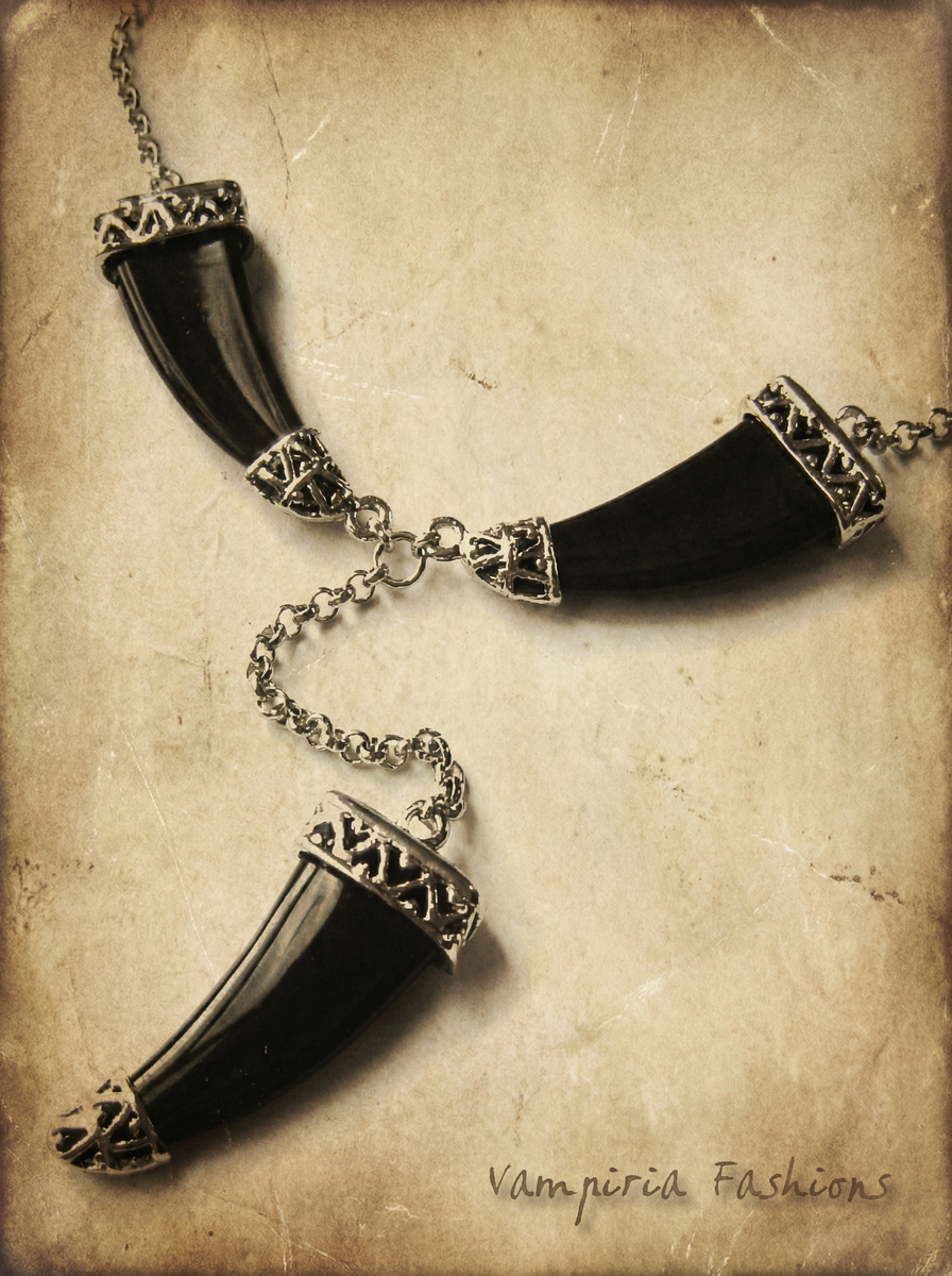 Schwarzes Collier mit drei tigerzahnförmigen Anhängern und silberfarbenen Zierelementen auf hellem Vintage-Hintergrund.