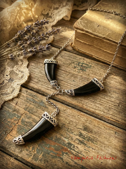 Schwarzes Tigerzahn-Collier mit drei Anhängern auf rustikalem Holztisch neben Buch, Spitze und Lavendel.