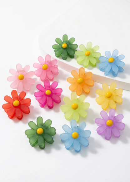 Farbig gemischte Mini-Haarklammern in Blumenform mit gelber Mitte auf weißem Hintergrund, teilweise einzeln angeordnet.