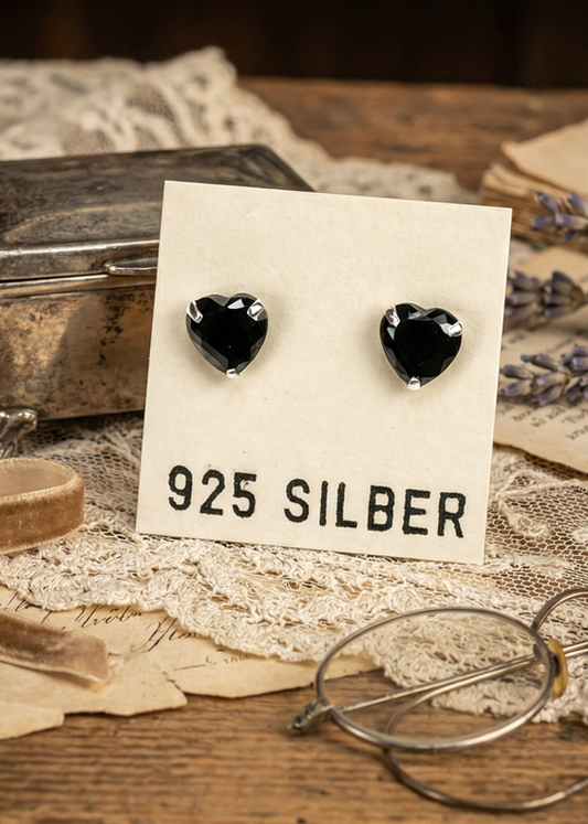 Herzförmige schwarze Ohrstecker aus 925 Silber auf Schmuckkarte mit Vintage-Hintergrund.