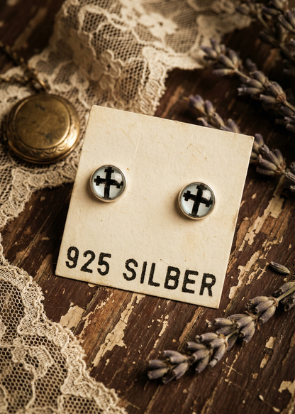 Ohrstecker mit schwarzem Kreuz-Motiv aus 925 Silber auf Vintage-Holzuntergrund.