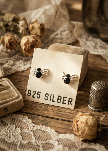 Spinnen-Ohrstecker aus 925 Silber mit schwarzen Details auf Schmuckkarte im Vintage-Stil.