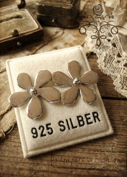 Silberfarbene Blumen-Ohrstecker auf Schmuckkarte mit Aufdruck „925 Silber“, Vintage-Foto auf Holzuntergrund.