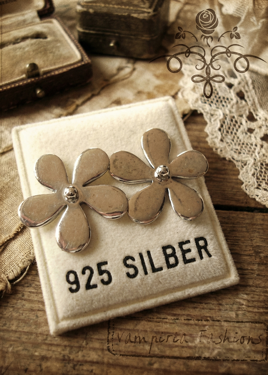 Silberfarbene Blumen-Ohrstecker auf Schmuckkarte mit Aufdruck „925 Silber“, Vintage-Foto auf Holzuntergrund.