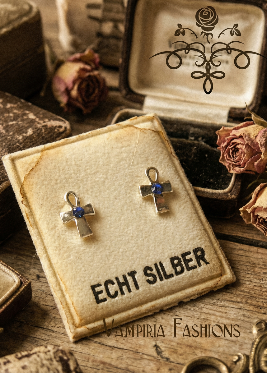 Zwei silberfarbene Mini-Ankh-Ohrstecker mit blauem Stein auf Schmuckkarte in Vintage-Dekoration.