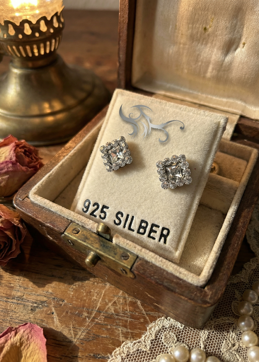 Mini Ohrstecker aus 925 Sterling Silber mit klarem quadratischem Kristall und Strasskranz auf Samtkärtchen in Schmuckschatulle, Aufdruck „925 SILBER“.