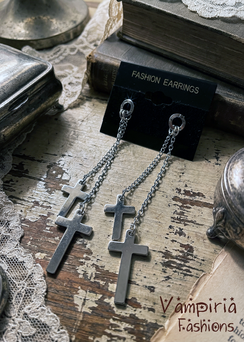 Silberfarbene Ohrstecker mit langen Kettchen und Kreuz-Anhängern auf schwarzer Schmuckkarte mit Aufdruck „Fashion Earrings“ auf vintage Holztisch mit Büchern und Spitzendekor.