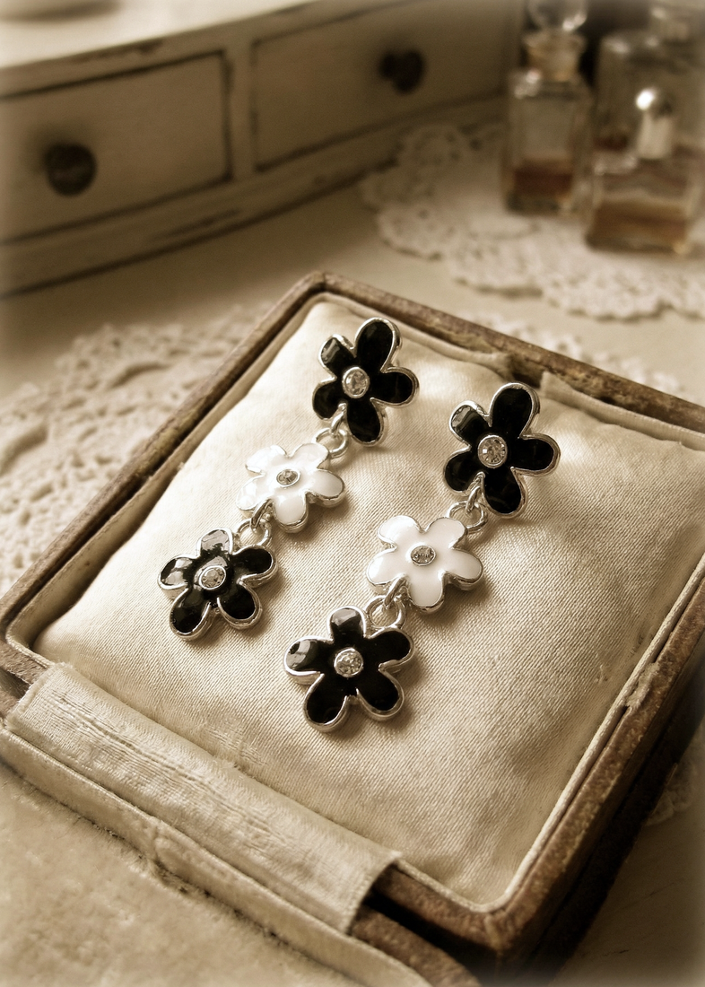 Schwarz-weiße Vintage-Blumenohrringe mit silberfarbenem Rand und kleinen klaren Steinen, präsentiert in einer geöffneten Schmuckschatulle auf hellem Stoff.