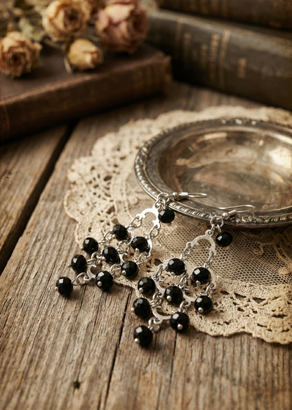 Zwei barocke Ohrhänger mit schwarzen facettierten Perlen auf einem silbernen Tablett im Vintage-Setting.