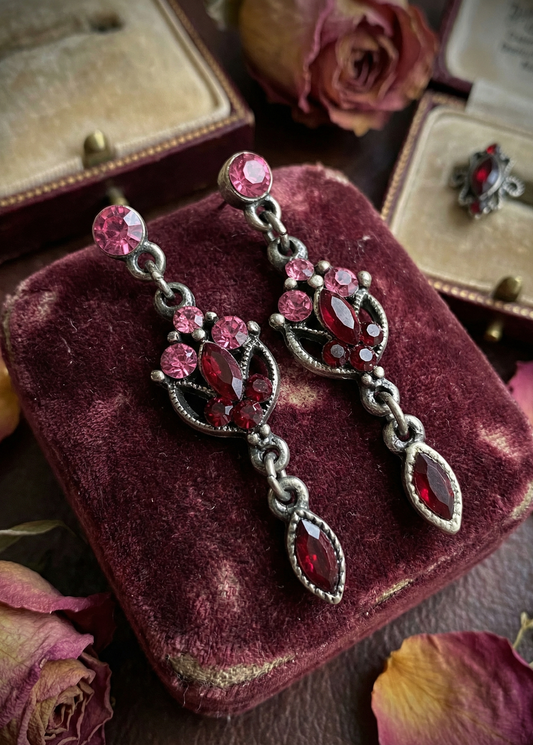 Vintage Ohrhänger mit pinken Ohrsteckern, roten Tropfensteinen und antik-silberfarbener Fassung auf bordeauxfarbenem Samtkissen.