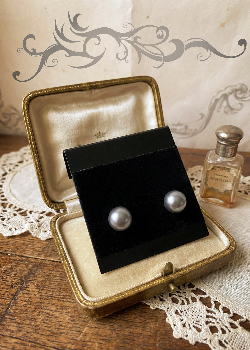 Graue Perlenohrstecker auf schwarzer Schmuckkarte in geöffnetem vintage Schmucketui auf Holztisch mit Spitze und kleinem Parfumflakon.