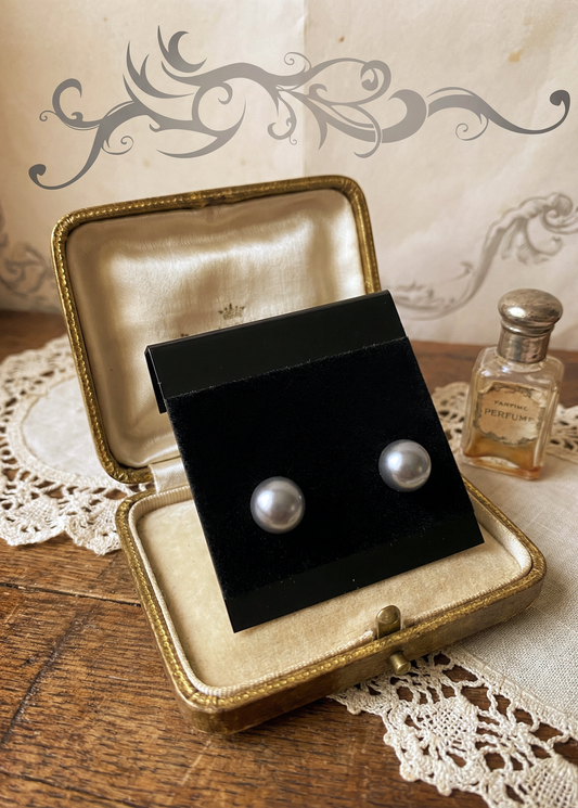 Graue Perlenohrstecker auf schwarzer Schmuckkarte in geöffnetem vintage Schmucketui auf Holztisch mit Spitze und kleinem Parfumflakon.